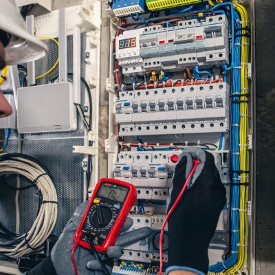 Man, an electrical technician working in a switchboard with fuses. Installation and connection of electrical equipment. Professional uses a tablet.